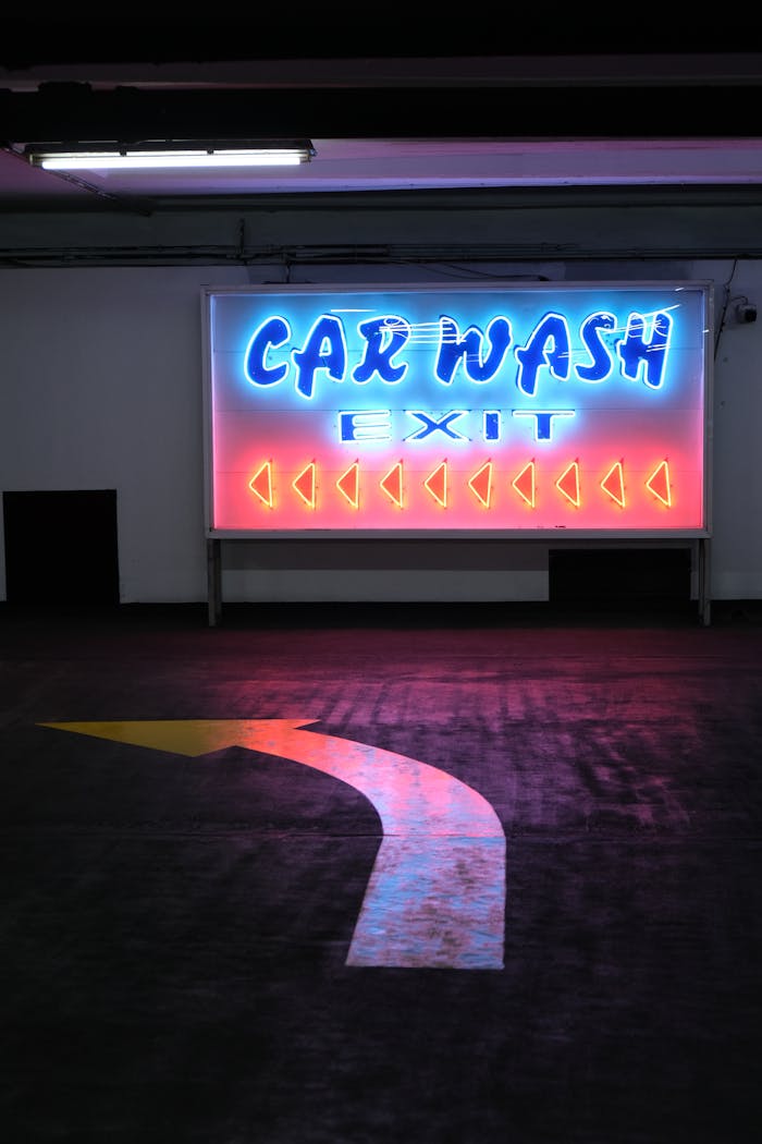 Neon car wash exit sign with directional arrow in an indoor parking area.